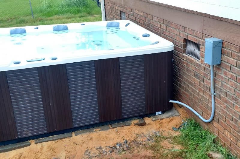 Outdoor hot tub with a dedicated electrical disconnect box mounted on the house